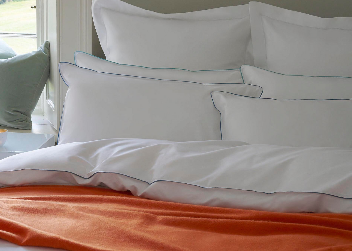 White bedding with orange blanket on a bed in a bedroom setting